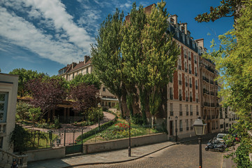 Apartment buildings and wooded gardens under sunny blue sky in a street of Montmartre at Paris. Known as the “City of Light”, is one of the most impressive world’s cultural center. Northern France.