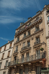 Fototapeta premium Balcony with flowers in a building facade and sunny day at Montmartre district in Paris. Known as the “City of Light”, is one of the most impressive world’s cultural center. Northern France.