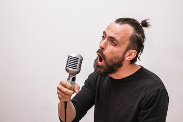 a man with a beard and a black t-shirt sings in a vintage chrome microphone
