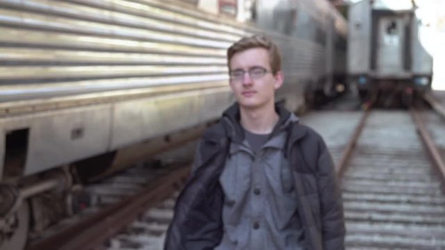Male strolling by while walking on railroad tracks near train.
