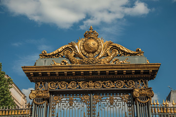 Detail of golden iron gate and fence lavishly decorated under sunny blue sky in Paris. Known as the “City of Light”, is one of the most impressive world’s cultural center. Northern France.