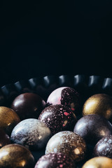 closeup view of pile of different chocolate candies in bowl on black background