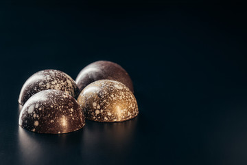 closeup image of chocolate candies with golden splashes on black background