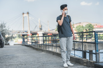 asian teen in protective mask talking by smartphone on bridge, air pollution concept