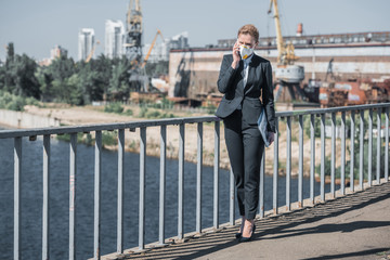 businesswoman in protective mask talking by smartphone on bridge, air pollution concept