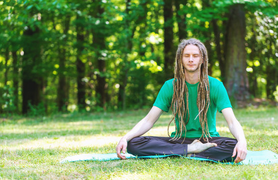 Man in a meditation pose outside in a field surrounded by forest - Powered by Adobe