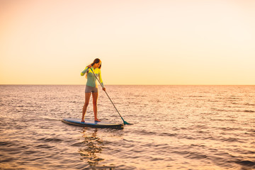 Sporty young woman stand up paddle surfing with beautiful sunset or sunrise colors