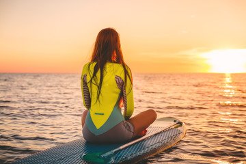 Woman relaxing on stand up paddle board, quiet sea with warm sunset colors.