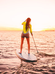 Attractive sporty woman stand up paddle surfing with beautiful sunset or sunrise colors