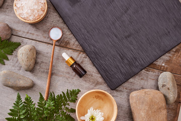 beauty product samples and bath salt with evergreen leaves and black stone on  wood table