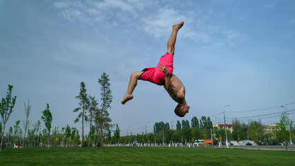 Tricking on lawn in park. Man does back flip and kick. Martial arts and parkour. Street workout.