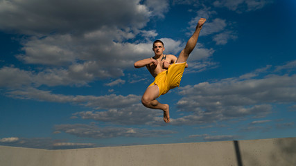 Obraz premium Tricking on street. Martial arts. Man does high kick in jump barefoot. Shooted from bottom foreshortening against sky.