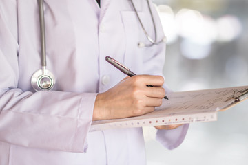 doctor with stethoscope on his neck writing prescription paper on clipboard
working at a hospital   