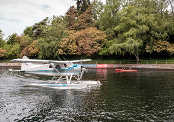 A float plane passes by a kayak with people in it on a narrow waterway
