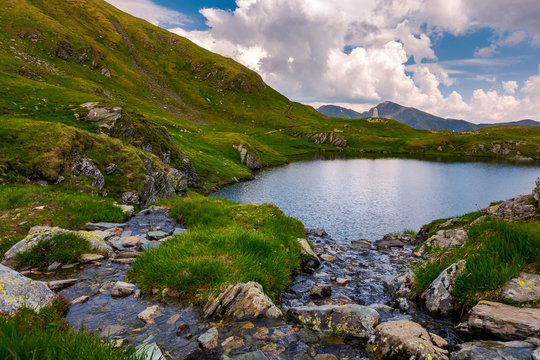 rapid streams flow to lake Capra in mountains. Fagaras mountain ridge under the gorgeous cloudscape in the distance. Beautiful summer landscape of Romania