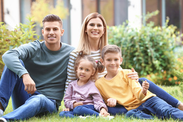 Obraz premium Happy family sitting on green grass in courtyard near their house