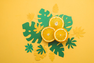 Fresh oranges with tropical leaves on a bright yellow background with copy space. Summer vacation flat lay with paper cutouts.