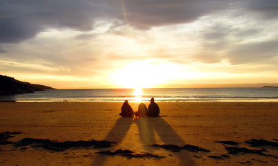 Three friends relaxing at the beach and watching a sunset