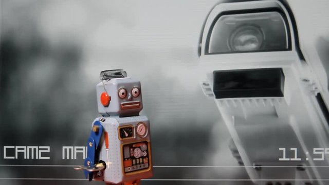 A neurotic tin toy robot walking over a screen showing a security cam watching the neighbors.
