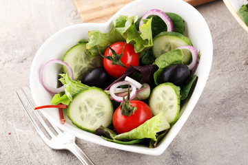 bowl of salad with vegetables and greens, with tomato, cucumber and onions.