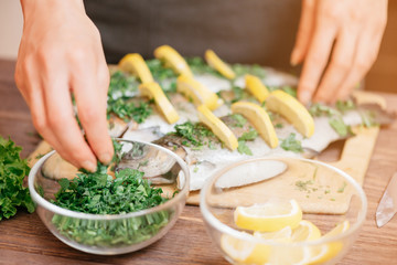 Female hands preparing fish with lemons and greenery.
