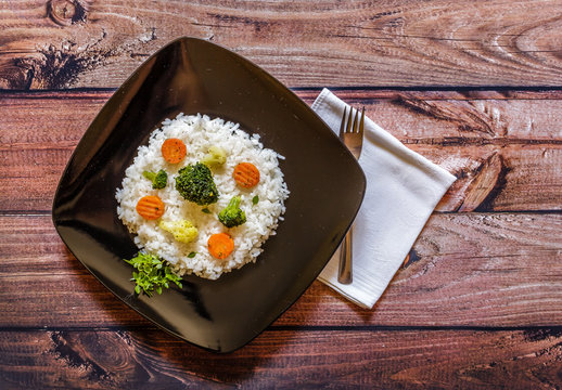 Black plate of rice with vegetable on wooden table