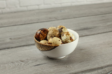 Spotted quail eggs in small porcelain bowl on gray wood desk.