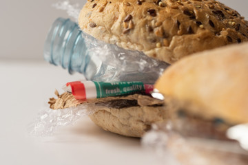 Fresh tasty burger with plastic waste and paper cardboard inside on white background. Recycled waste in our food concept