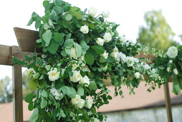 Rustic Wedding Ceremony Arch on the Open Area with Greem Grass. Wooden Arch with Flowers Arrangement