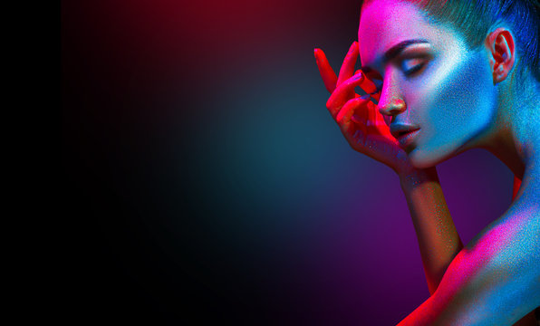 Fashion model woman in colorful bright sparkles and neon lights posing in studio, portrait of beautiful sexy girl. Art design colorful vivid makeup