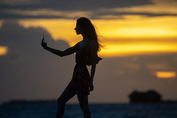 Fototapeta premium Girl in a dress, on the shore of the ocean, makes a selfie
