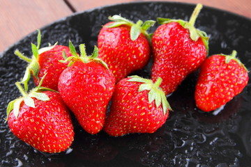 Strawberries on a black plate top view, red berries on a wooden background, fresh strawberries on dark wooden boards, vegetarian food, copy space