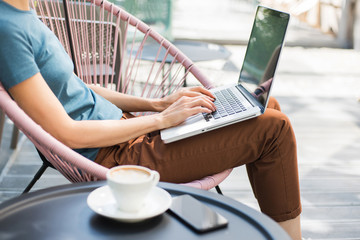 Young woman using laptop outdoor. Beautiful girl sitting in a coffee shop terrace and working on computer
