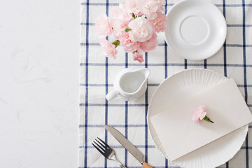 Table setting with dishes, cutlery and flowers on white background