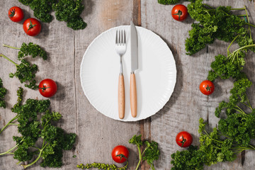 Fresh seasonal organic vegetables,ingredients cutlery and kitchen checked napkin on light rustic background, top view, frame. Healthy eating or clean food concept.