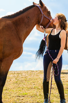 Jockey young girl kissing and hugging brown horse