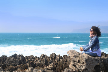 Fototapeta na wymiar Beautiful curly girl sitting on a rock on the ocean background