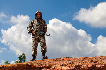 man in camouflage uniform with a weapon in the desert.