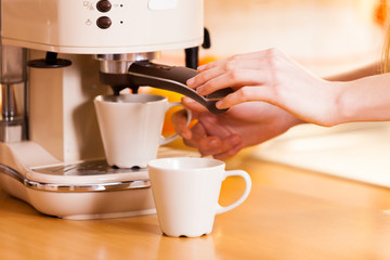 Woman in kitchen making coffee from machine
