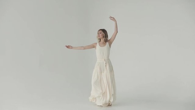 A ballerina in a light long fluttering dress and pointe shoes is dancing classical ballet.