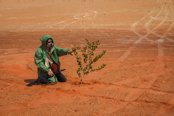 Fototapeta premium man in a chemical protection suit with arms in the desert. concept survivor after the war. cares for a tree sprout