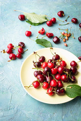 organic cherries in a dish and scattered on rustic wooden background. Top view