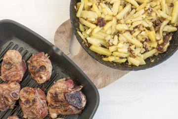 Fried homemade potatoes and grilled meat frying pan on a light wooden background