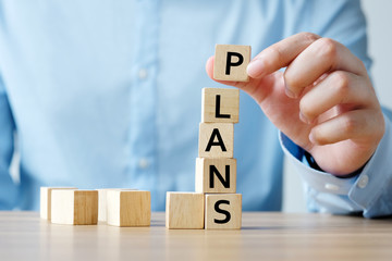 Man hand holding wooden cube with plans word on table background, success in business concept