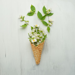 Flat spoons sweet cone waffle with white flowers on a light background background, top view. The concept of spring or summer mood
