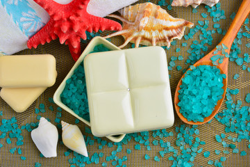 Blue sea salt for spa treatments in a white square ceramic box with a lid, next to white terry towels, a red starfish and seashells