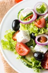 Fresh Greek salad made of cherry tomato, ruccola, arugula, feta, olives, cucumbers, onion and spices. Caesar salad in a white bowl on wooden background. Healthy organic diet food concept.