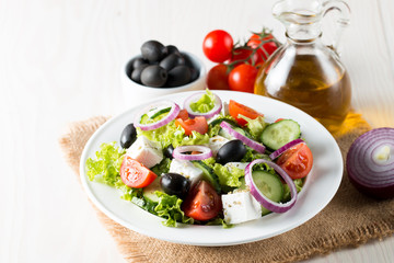 Fresh Greek salad made of cherry tomato, ruccola, arugula, feta, olives, cucumbers, onion and spices. Caesar salad in a white bowl on wooden background. Healthy organic diet food concept.