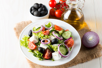 Obraz na płótnie Canvas Fresh Greek salad made of cherry tomato, ruccola, arugula, feta, olives, cucumbers, onion and spices. Caesar salad in a white bowl on wooden background. Healthy organic diet food concept.