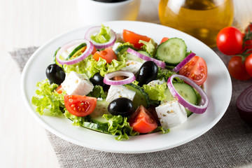 Fresh Greek salad made of cherry tomato, ruccola, arugula, feta, olives, cucumbers, onion and spices. Caesar salad in a white bowl on wooden background. Healthy organic diet food concept.